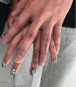 Couple's hands showing matching minimalist tattoos of a heart and key, symbolizing love and connection, with stylish nail art.